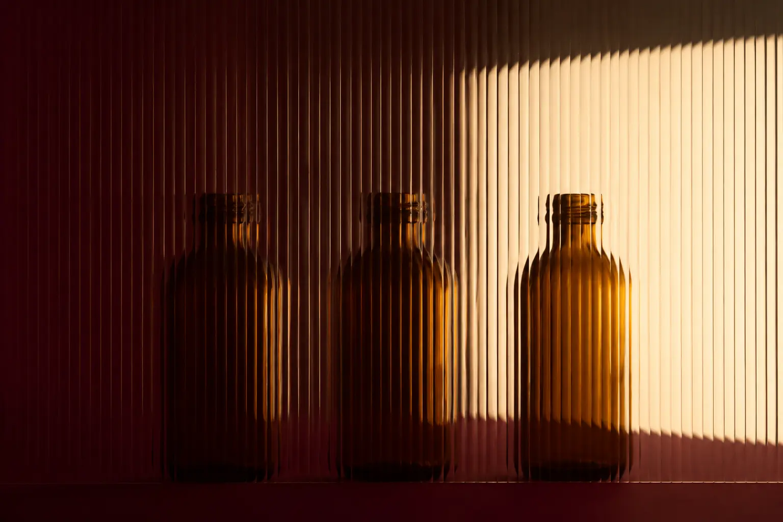 Three anonymous amber bottle silhouettes behind fluted glass